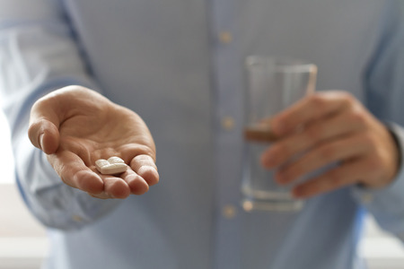 Closeup view of man holding pills in one hand and glass of water in the another handの写真素材