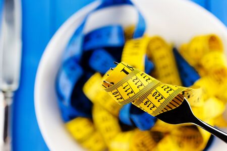 Healthy lifestyle concept. Closeup view of fork with measuring tape over the plate with knife on...