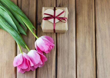 Pink tulips and gift box with bow on wooden background with place for your textの写真素材