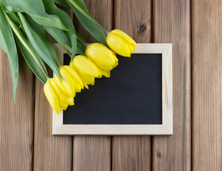 Top view of yellow tulips with blank blackboard on wooden backgroundの写真素材