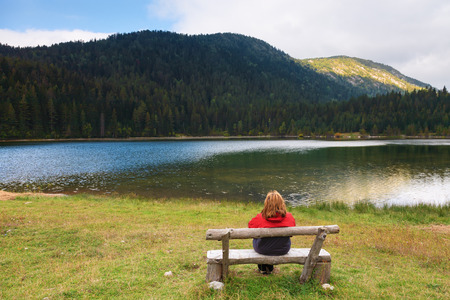 Lonely woman sits on a bench and watching the mountain Lakeの写真素材