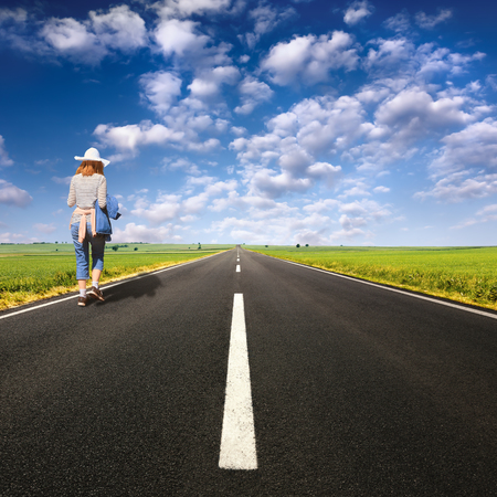 Lonely girl with hat on open asphalt road at nice sunny dayの写真素材