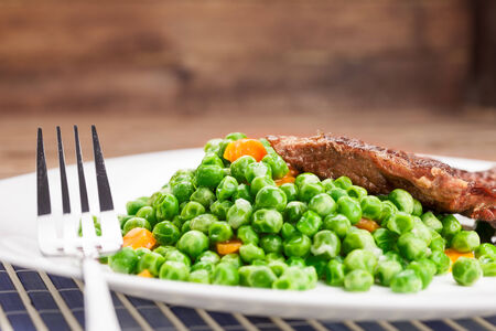 Grilled beef steak with cooked peas and carrot の写真素材