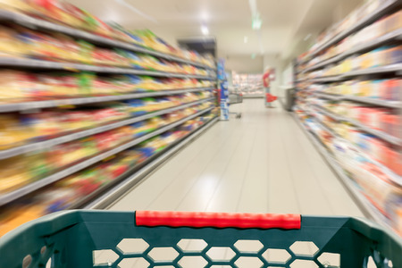 Shopping concept in supermarket for fast consumer lifestyle. Shopping cart in in blurred motion through the aisles.の写真素材