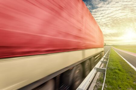 Red truck in motion blur at full speed passing by on the highway towards the setting sun.の写真素材