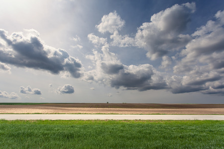 Side view of empty asphalt road and cultivated fields at idyllic sunny day.の写真素材