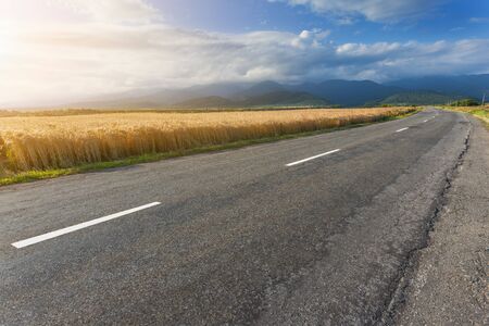 Driving on an empty asphalt road towards the mountains through wheat fields at sunny morning. Tranfagarasan road, Romania.の写真素材