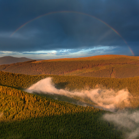 Mountain landscape with woods layers and rainbow in background illuminated by setting sun. Wild Parang mountains after the storm in Romania.の写真素材