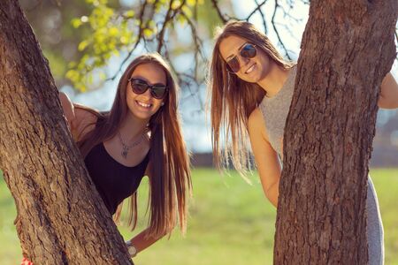 Friendship - lifestyle concept. Group of young and cheerful girls having fun and peeking behind the tree.の写真素材