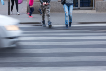 Busy city street with people and car in motion blur on crosswalk. Dangerous scene with disregard of traffic regulations. Speed concept.の写真素材