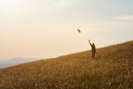 Happy woman enjoying the nature in vastness, feel free and throwing her hat in the air toward the setting sun. Lifestyle and celebration concept.の写真素材