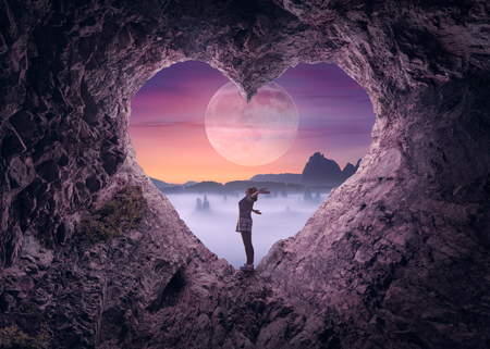 Young woman enjoying in beautiful night mountain nature, celebrating freedom and rising her arms while standing toward the big moon. Valentines day concept.の写真素材