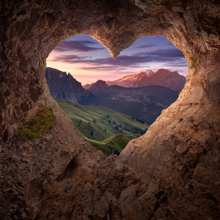 Beautiful mountain landscape from hearth shaped entrance of rocky cave at sunrise. Valentines day concept.の写真素材