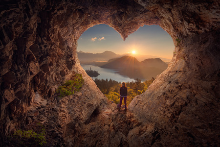 Lone woman enjoying in beautiful mountain nature, celebrating freedom and standing on edge of the cliff against the rising sun. Valentines day concept.の写真素材