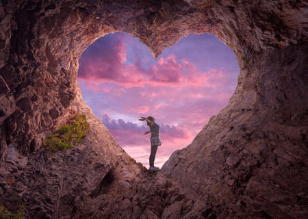 Happy woman enjoying in idyllic mountain nature, celebrating freedom and rising her arms while standing toward the setting sun. Valentines day concept.の写真素材