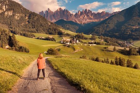 Lone woman standing on the alpine road and watching beautiful Dolomites mountain scenery at idyllic...