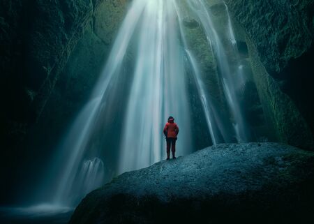 Iceland landscape photo of brave woman standing on slippery rock towards waterfall in mossy cave at spooky atmospere.の写真素材