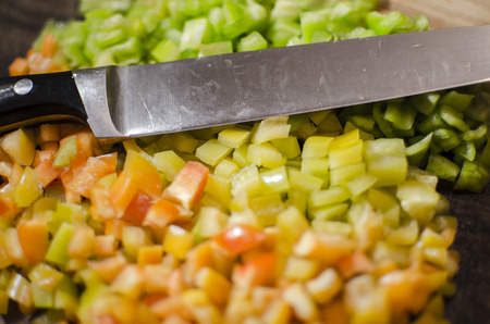 Red, green and yellow pepper dices with knifeの写真素材