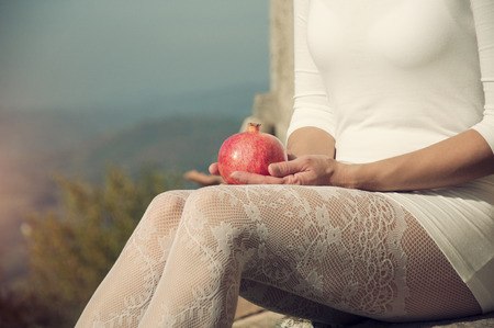Woman in white lace stockings holding pomegranate in her handsの写真素材