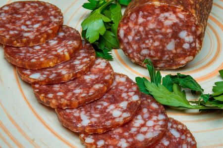 Smoked sausage salami sliced on a plate with greens.