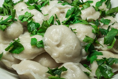Boiled prepared homemade russian dumplings or pelmeni with beef meat on the white plate with fresh parsley and black pepper.の写真素材