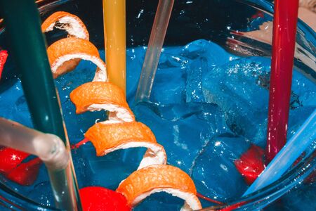 Tasty big blue cocktail with ice, cherries and an orange with a straw close-up