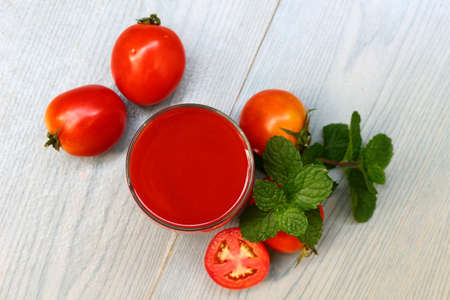 Glass of tomato juice with fresh tomatoes and mint leaves on wooden .の素材