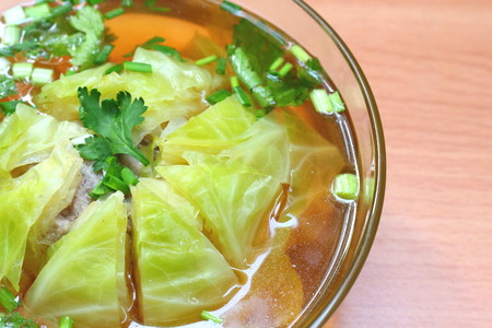 Cabbage soup in glass bowl on wooden background. One kind of local Thai food. Ingredient : fresh cabbage, sliced coriander, sliced onion plant, and ground pork. Seasoning with sugar and fish sauce.の写真素材