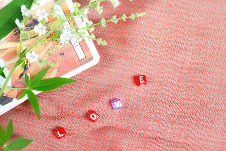 Plastic square in the word of love,fresh flowers and blurred tarot cards on soft red cloth, love and tarot concept look from top view in theme of love and fortune.の写真素材