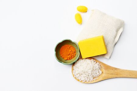 Setting of turmeric soap with turmeric powder in small bowl, flower of salt on wooden paddle, two yellow silkworms on soap cloth bag on white background.の写真素材