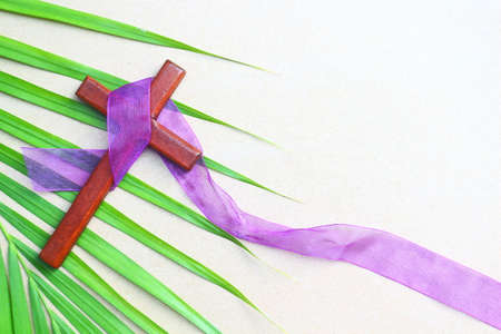 Vintage wooden cross on purple cloth ribbon and green palm leaf.の写真素材