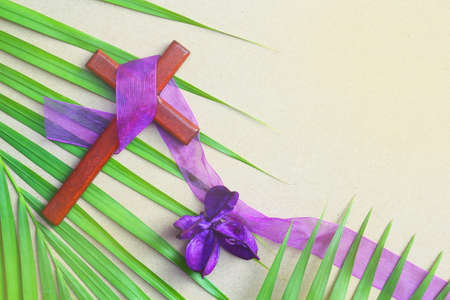 Vintage wooden cross on purple cloth ribbon decorated with green palm leaf and dried flowers. Purple is symbolic color of Lent.の写真素材