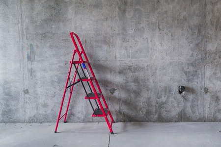 Red ladder on concrete wall. Renovation and construction concept. Copy space.の写真素材