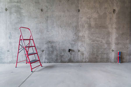 Red ladder on the gray concrete wall background. Repair and renovation concept.の写真素材