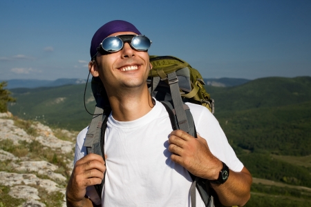 Tourist male looking on the sun and smilling  Mirror sunglasses, white t-shirt, green rucksack  Close up  Top of mountains の写真素材