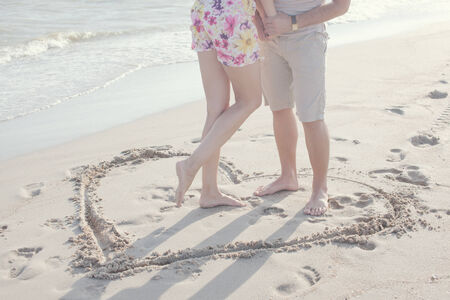 A heart shape drawn in the sand. Couple standing inside heart picture on the sand. Summertime funの写真素材
