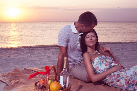 Passion couple on the beach sunset. Man kissing young woman on the forehead. Picnic with wine and fruitsの写真素材