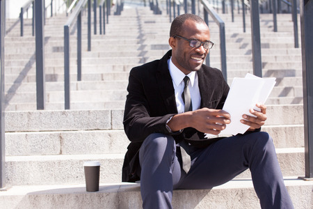 happy black businessman sitting with coffee and documents handlingの写真素材