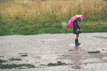 Little girl playing alone outside in bad weather. Summer rainの写真素材