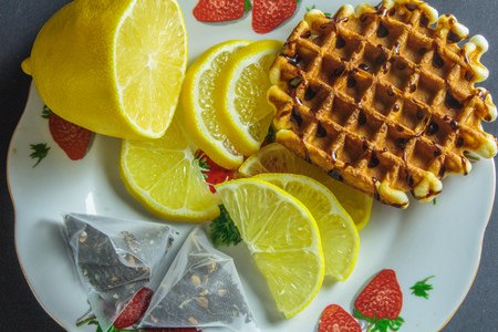 Viennese waffles topped with chocolate and sliced lemon in a plate on a dark backgroundの写真素材