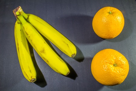 Bananas and oranges on a dark gray background.の写真素材