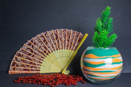 Chinese fan, vase with colored sand and spruce branch on the dark backgroundの写真素材