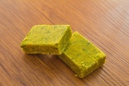 Dehydrated bouillon stock cube salty meat and vegetables aromatic yellow spice, ingredient single whole condiment portion wrapped, open in paper pack on wooden backgroundの写真素材