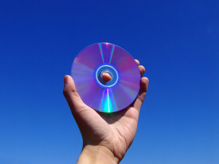 Hand holding dvd disk against blue skyの写真素材