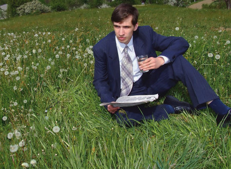 Yound businessman sits on a lawn and holds newspaperの写真素材