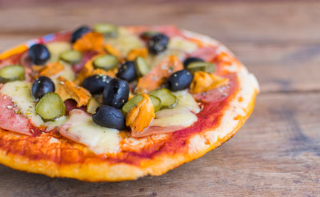 Homemade pizza with tomato sauce, cheese , olives , ham and mushrooms on wooden table. Selective focusの写真素材