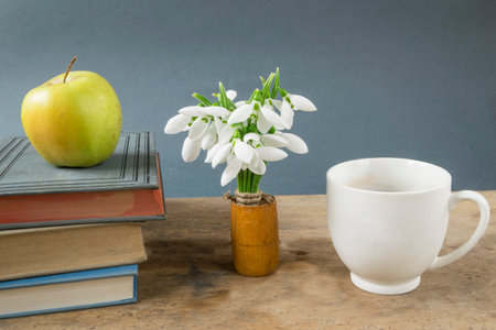Creative book arrangement with apple and snowdrops on wooden tableの写真素材
