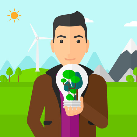 A man standing on a background with wind turbins and holding in hands a big lightbulb with trees inside vector flat design illustration. Square layout.のイラスト素材