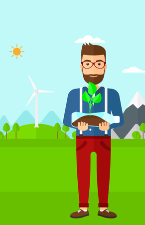 A hipster man with the beard standing on a background with wind turbins and holding in hands a plastic bottle with a small plant growing inside vector flat design illustration. Vertical layout.のイラスト素材