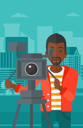 An african-american cameraman looking through movie camera on a city background vector flat design illustration. Vertical layout.のイラスト素材